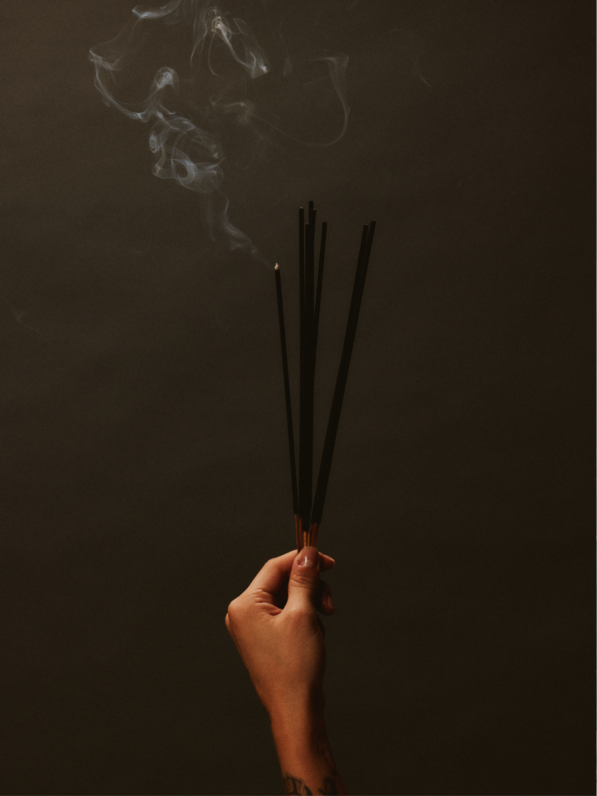 Hand holding burning incense sticks with rising smoke, representing mindfulness, reflection, and emotional grounding.