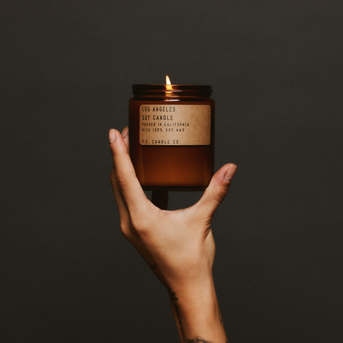 Hand holding a lit los angeles standard candle with a label against a dark background