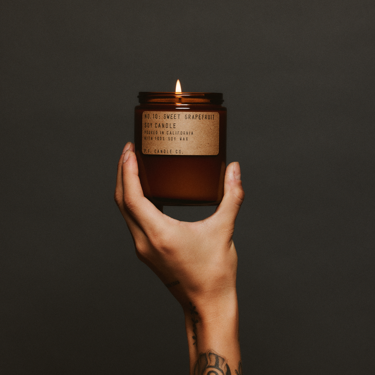 Hand holding a lit sweet grapefruit standard candle with a label against a dark background