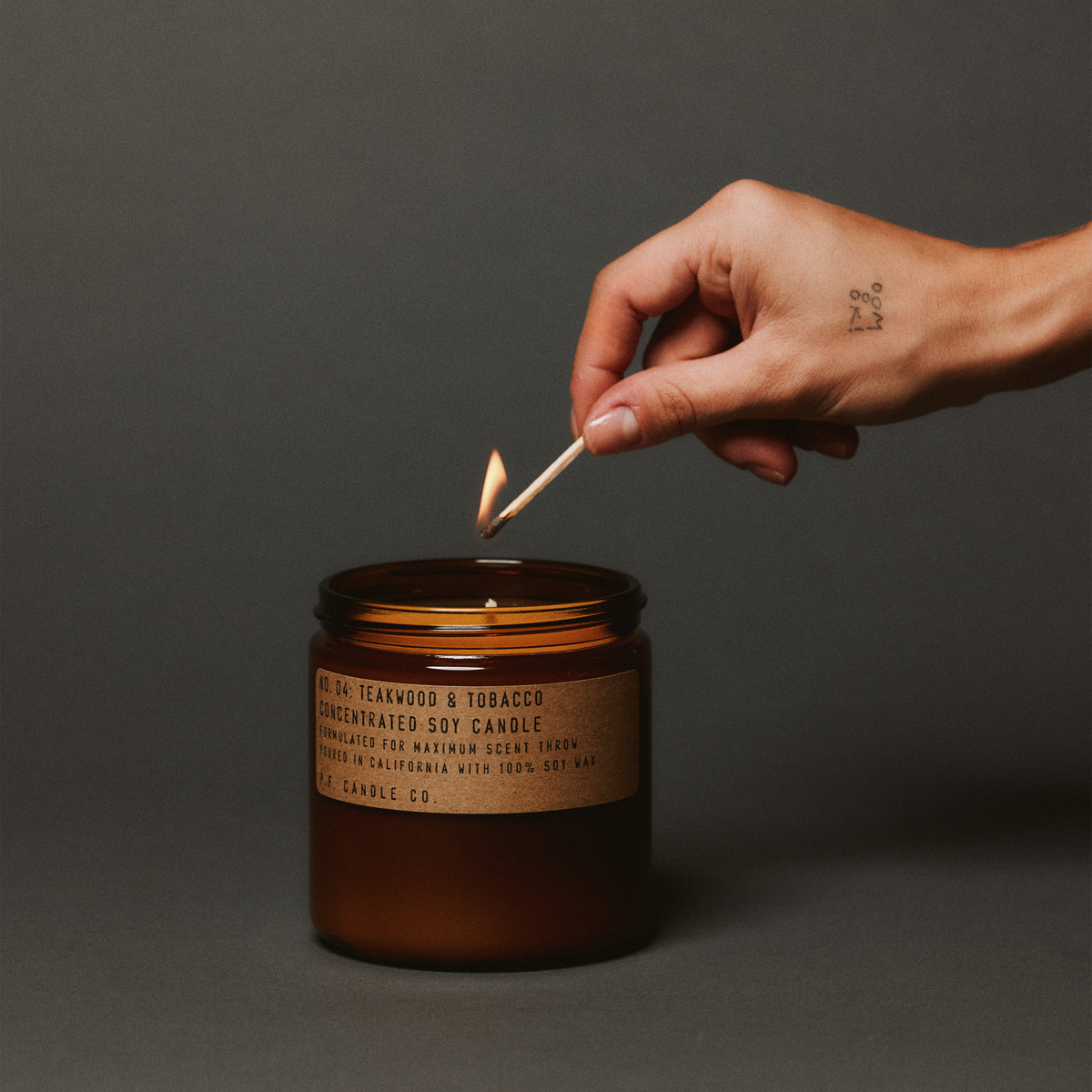 teakwood & tobacco large concentrated candle being lit up with match in hand 